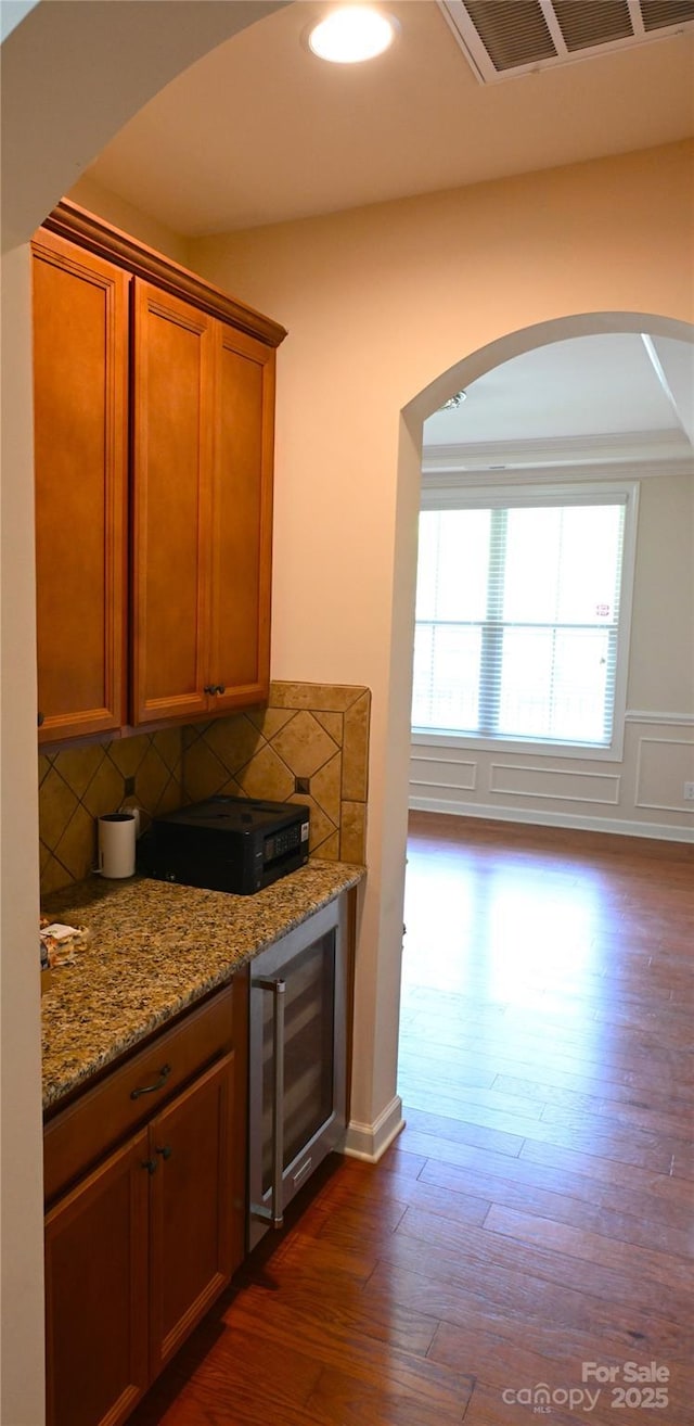 bar area with beverage cooler, dark wood finished floors, decorative backsplash, and arched walkways