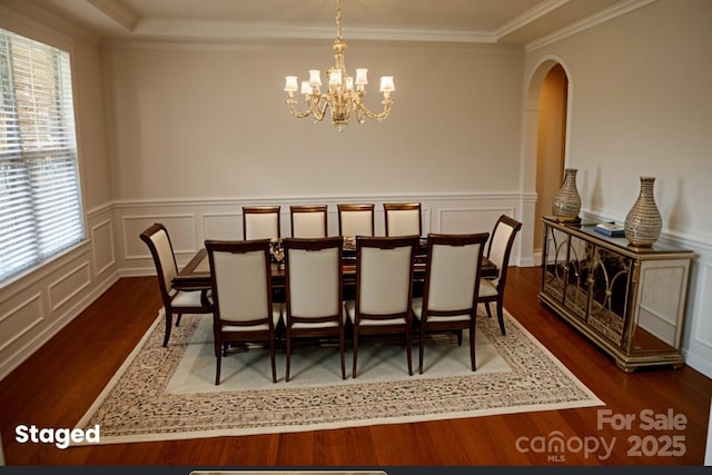 dining area featuring wood finished floors, a decorative wall, a chandelier, crown molding, and arched walkways