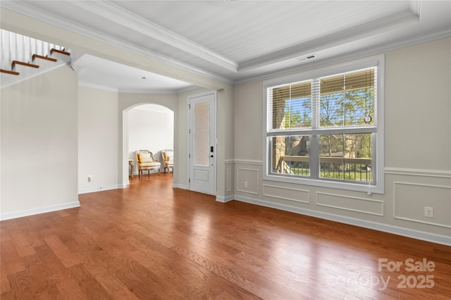 unfurnished room with arched walkways, wood finished floors, crown molding, and wainscoting