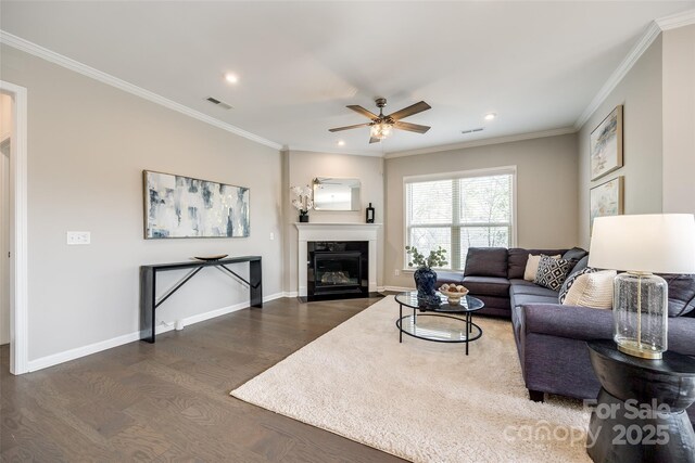 living area featuring visible vents, crown molding, baseboards, wood finished floors, and a ceiling fan