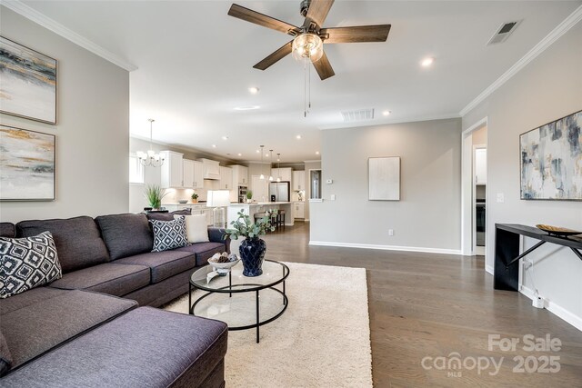 living area with ceiling fan with notable chandelier, crown molding, dark wood-type flooring, and visible vents