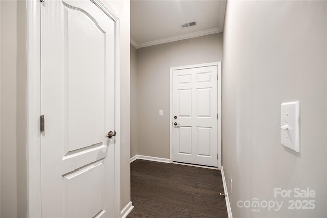 hallway with dark wood finished floors, baseboards, visible vents, and ornamental molding