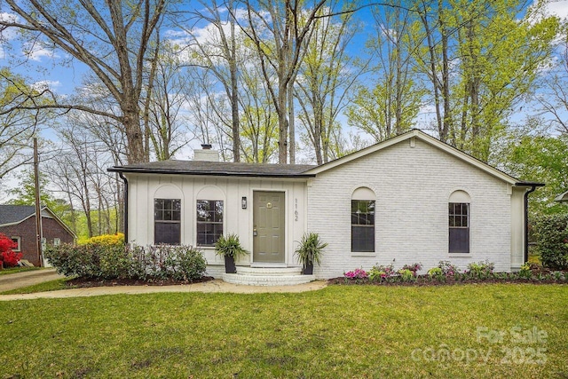 single story home featuring a chimney, brick siding, board and batten siding, and a front lawn