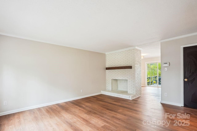 unfurnished living room featuring a brick fireplace, crown molding, baseboards, and wood finished floors