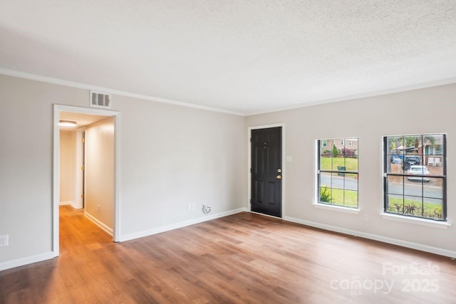 unfurnished room with baseboards, visible vents, wood finished floors, and ornamental molding