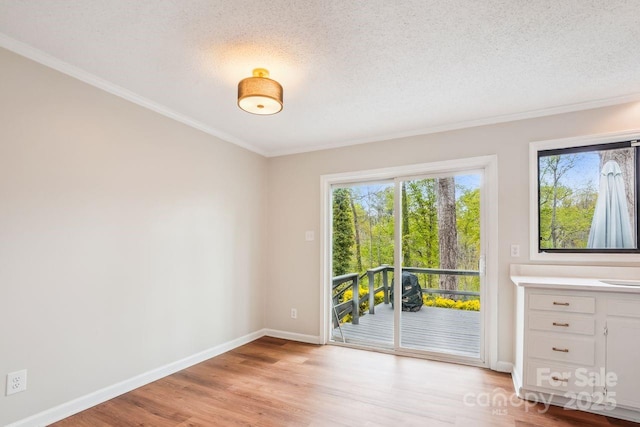 spare room featuring baseboards, light wood-type flooring, crown molding, and a textured ceiling