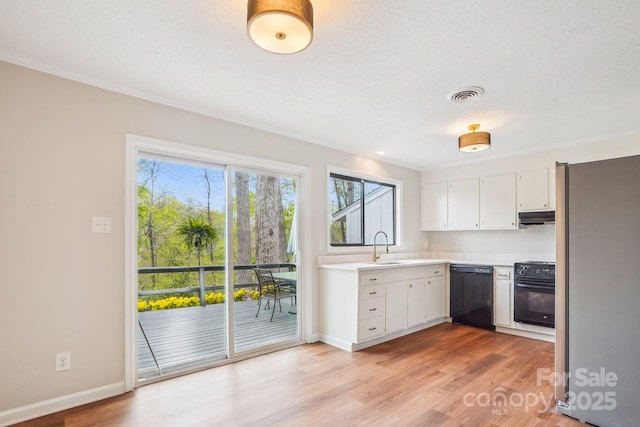 kitchen featuring light countertops, white cabinets, under cabinet range hood, visible vents, and black appliances