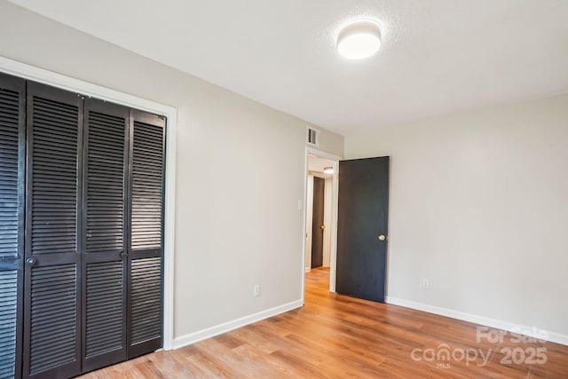unfurnished bedroom featuring light wood-style flooring, baseboards, a closet, and visible vents
