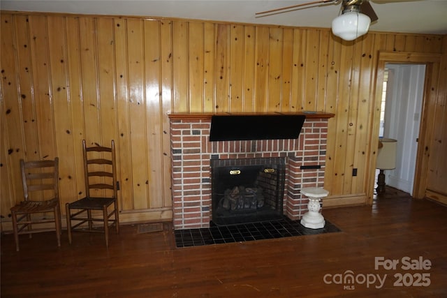living area with wood finished floors, ceiling fan, a fireplace, baseboards, and wooden walls