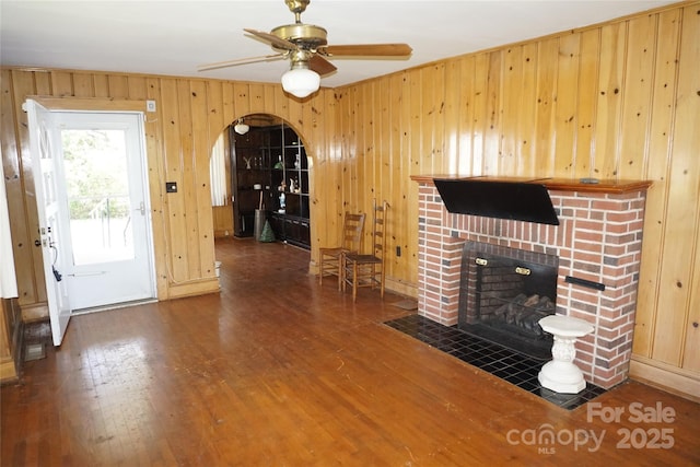unfurnished living room with a fireplace, wood finished floors, ceiling fan, and arched walkways
