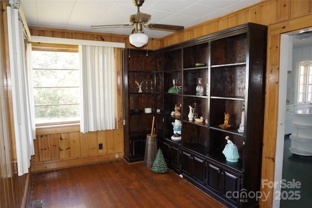 interior space featuring wooden walls, dark wood-style floors, ceiling fan, and visible vents