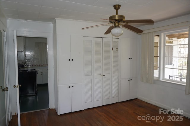 unfurnished bedroom with a closet, ceiling fan, ensuite bath, baseboards, and dark wood finished floors