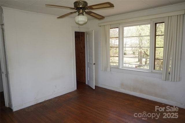 empty room with a wealth of natural light, a ceiling fan, dark wood finished floors, and baseboards