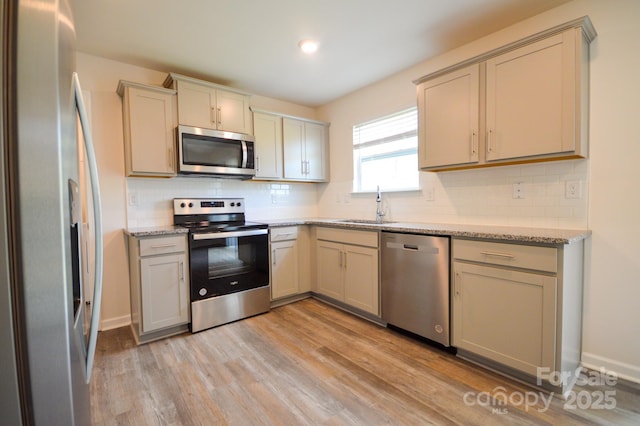 kitchen with a sink, light stone countertops, decorative backsplash, light wood-style flooring, and appliances with stainless steel finishes