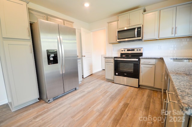 kitchen featuring light stone countertops, decorative backsplash, light wood-style floors, and appliances with stainless steel finishes