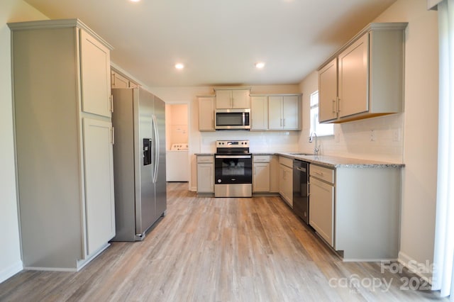 kitchen with stainless steel appliances, a sink, light wood-style floors, washer / clothes dryer, and light stone countertops