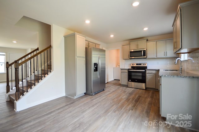 kitchen featuring light stone counters, wood finished floors, a sink, baseboards, and appliances with stainless steel finishes