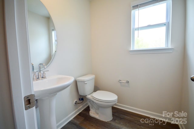 half bathroom with wood finished floors, toilet, and baseboards