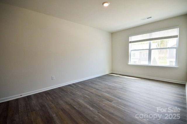 unfurnished room featuring dark wood-type flooring, visible vents, and baseboards