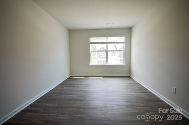 empty room featuring visible vents, baseboards, and dark wood-style floors
