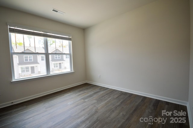 empty room featuring dark wood-type flooring, visible vents, and baseboards