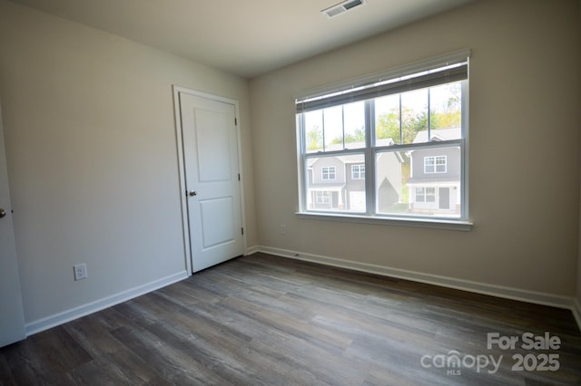 unfurnished room featuring dark wood-type flooring, visible vents, and baseboards