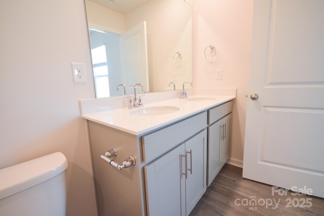 bathroom featuring double vanity, wood finished floors, toilet, and a sink