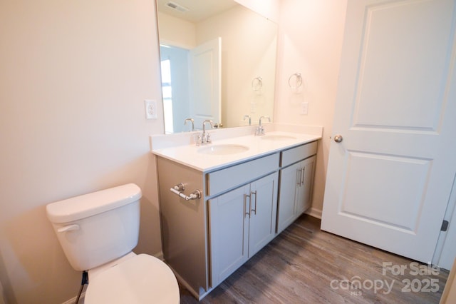 bathroom featuring toilet, wood finished floors, a sink, and double vanity