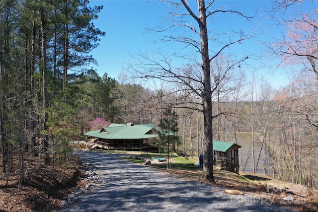 view of street with a wooded view and gravel driveway
