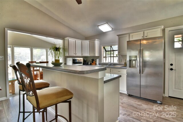 kitchen with dark countertops, stainless steel fridge, light wood finished floors, a kitchen bar, and lofted ceiling