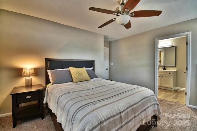 bedroom featuring baseboards, ensuite bath, light colored carpet, and a sink