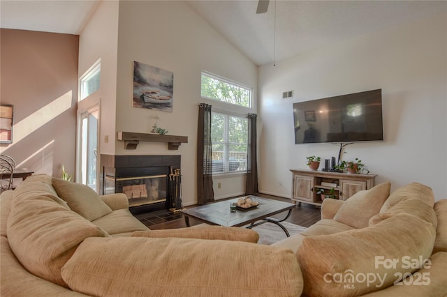 living area with high vaulted ceiling, visible vents, a tiled fireplace, a ceiling fan, and wood finished floors