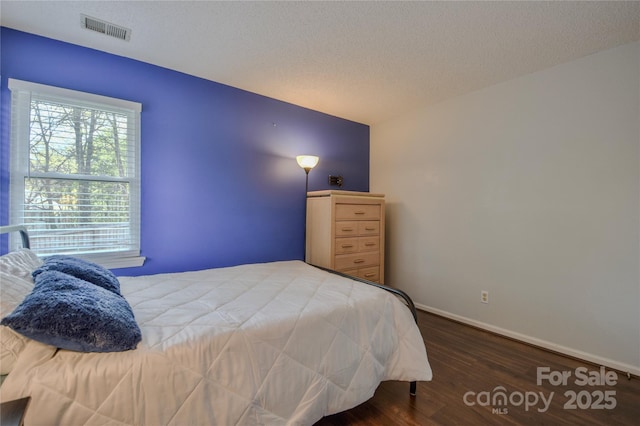 bedroom featuring wood finished floors, a textured ceiling, baseboards, and visible vents