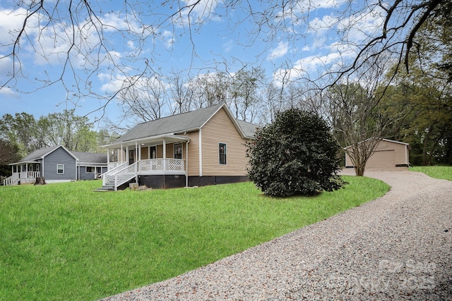 view of side of property with an outbuilding, a yard, a detached garage, a porch, and driveway