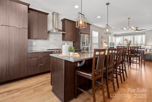 324 Uptown W Dr, Charlotte, NC 28208 - kitchen with light wood-style flooring, stainless steel fridge with ice dispenser, a breakfast bar area, wall chimney range hood, and an inviting chandelier