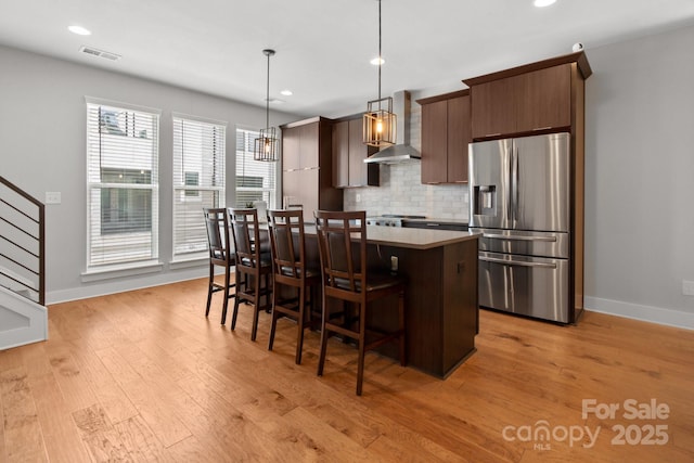 324 Uptown W Dr, Charlotte, NC 28208 - kitchen featuring a kitchen island, a breakfast bar, stainless steel refrigerator with ice dispenser, wall chimney range hood, and visible vents