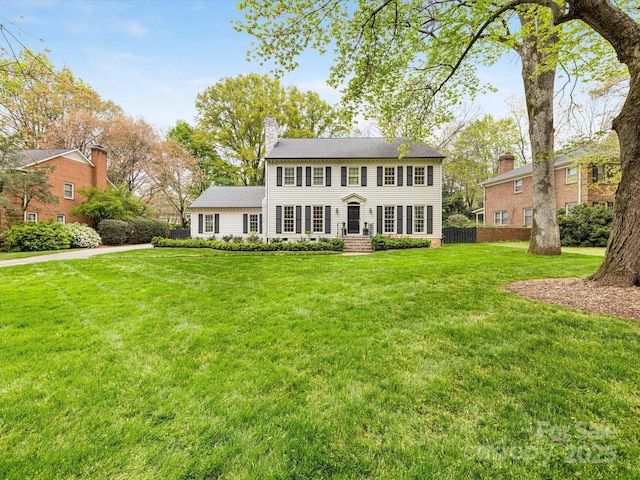 view of front facade with a front lawn, a chimney, and fence