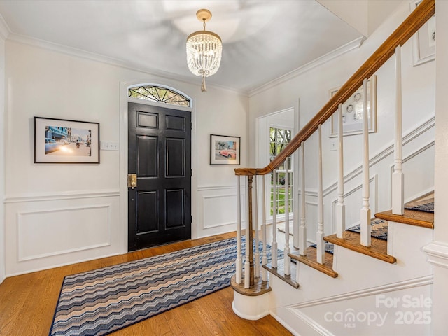 entryway featuring a wainscoted wall, stairs, a notable chandelier, wood finished floors, and ornamental molding