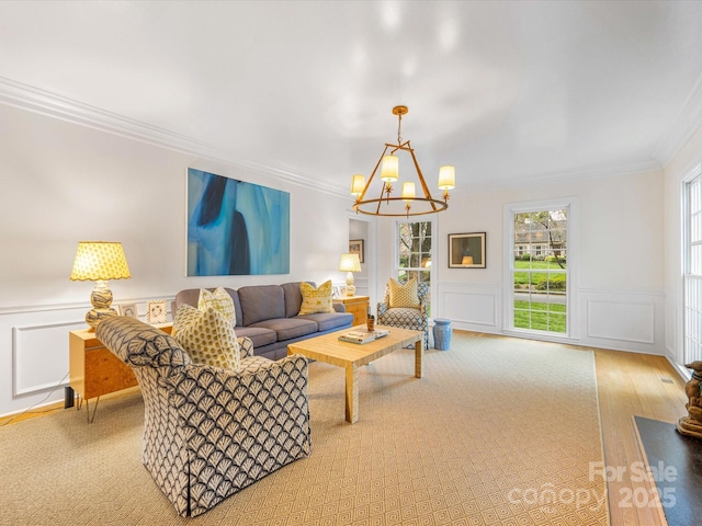 living room with a decorative wall, an inviting chandelier, crown molding, and wainscoting