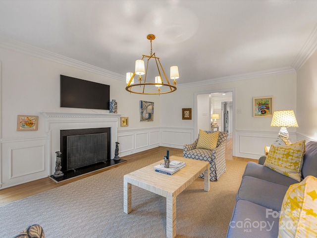 living area with a fireplace with raised hearth, a decorative wall, ornamental molding, and a chandelier