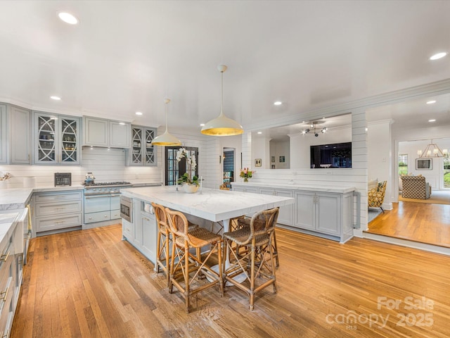 kitchen featuring light wood finished floors, gray cabinetry, light stone counters, and glass insert cabinets