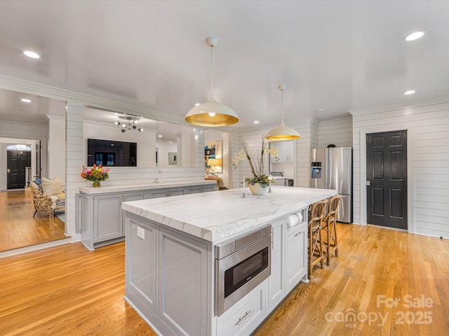 kitchen featuring a kitchen bar, decorative light fixtures, a kitchen island, light wood finished floors, and appliances with stainless steel finishes