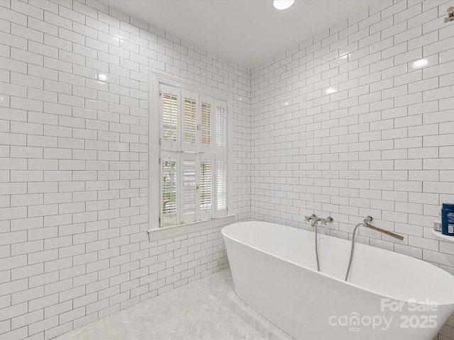 full bathroom with tile patterned flooring, a freestanding tub, and tile walls