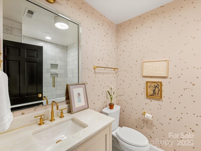 bathroom with vanity, toilet, a shower with door, wallpapered walls, and visible vents