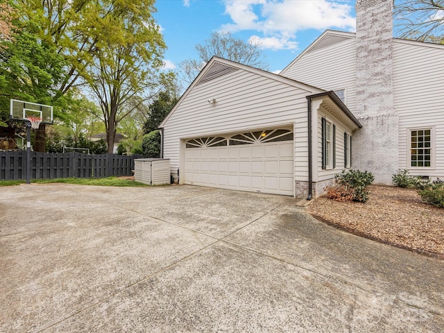 view of home's exterior featuring driveway, a garage, fence, and a chimney