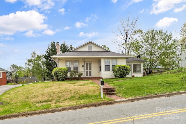view of front of home with a front yard, a porch, a shingled roof, and a chimney