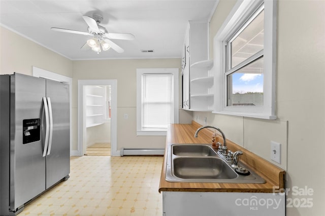 kitchen with stainless steel fridge, white cabinets, light floors, a baseboard radiator, and a sink