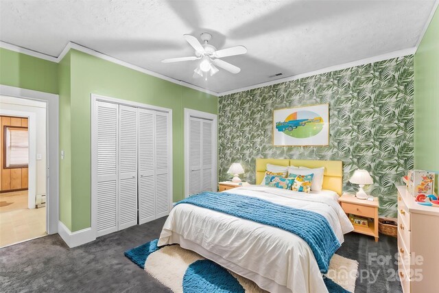 carpeted bedroom featuring visible vents, baseboards, two closets, ornamental molding, and wallpapered walls