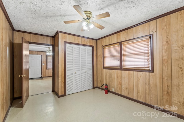 unfurnished bedroom featuring a closet, baseboards, wooden walls, a textured ceiling, and crown molding