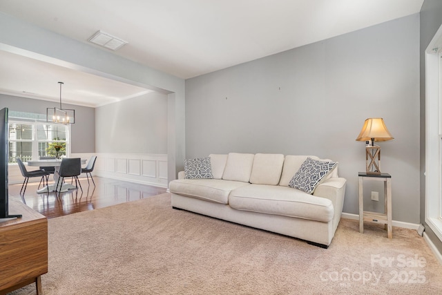 carpeted living room with a decorative wall, a notable chandelier, visible vents, and a wainscoted wall